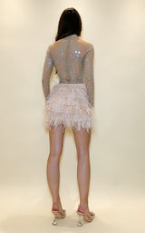 Woman wearing a sparkling dress with long sleeves and feather details on a plain background
