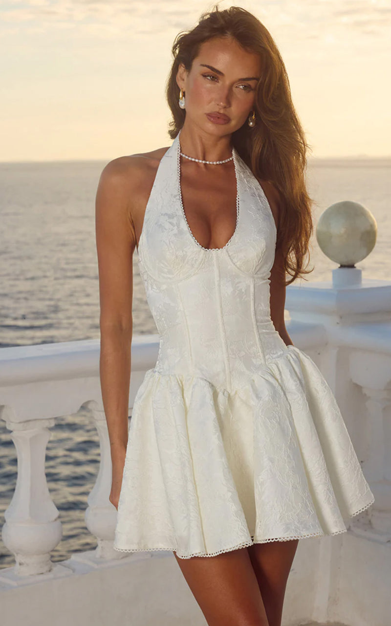 Woman wearing a white lace bridal mini dress by a scenic coastal setting