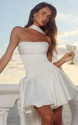 Woman in a white modern hen do dress holding a seashell champagne glass on a beach background sunset sky.