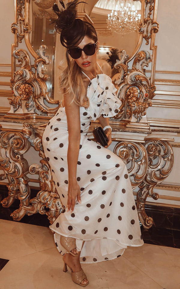 Woman in a white polka dot dress standing in front of an ornate mirror.
