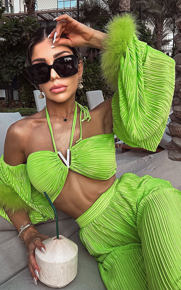 Woman in a bright green outfit holding a coconut, tropical environment background.